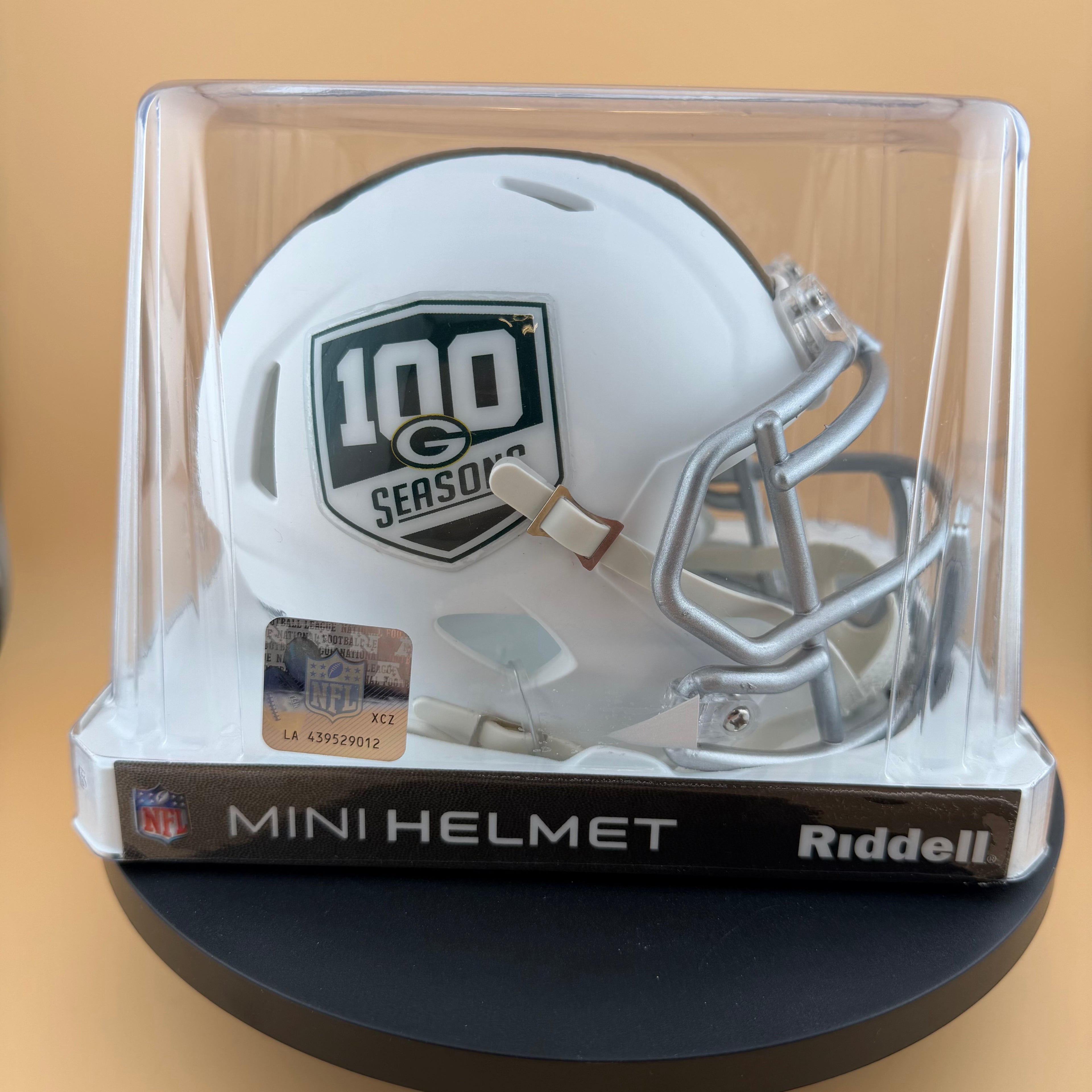 White mini football helmet with '100th Season' logo in a clear display case on a beige background