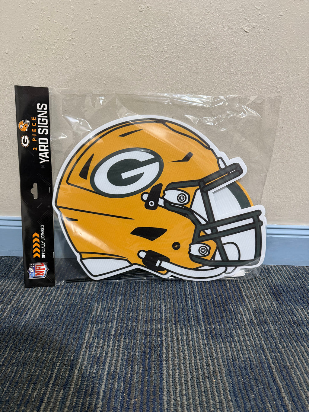 Green Bay Packers helmet yard sign in packaging on a carpeted floor.