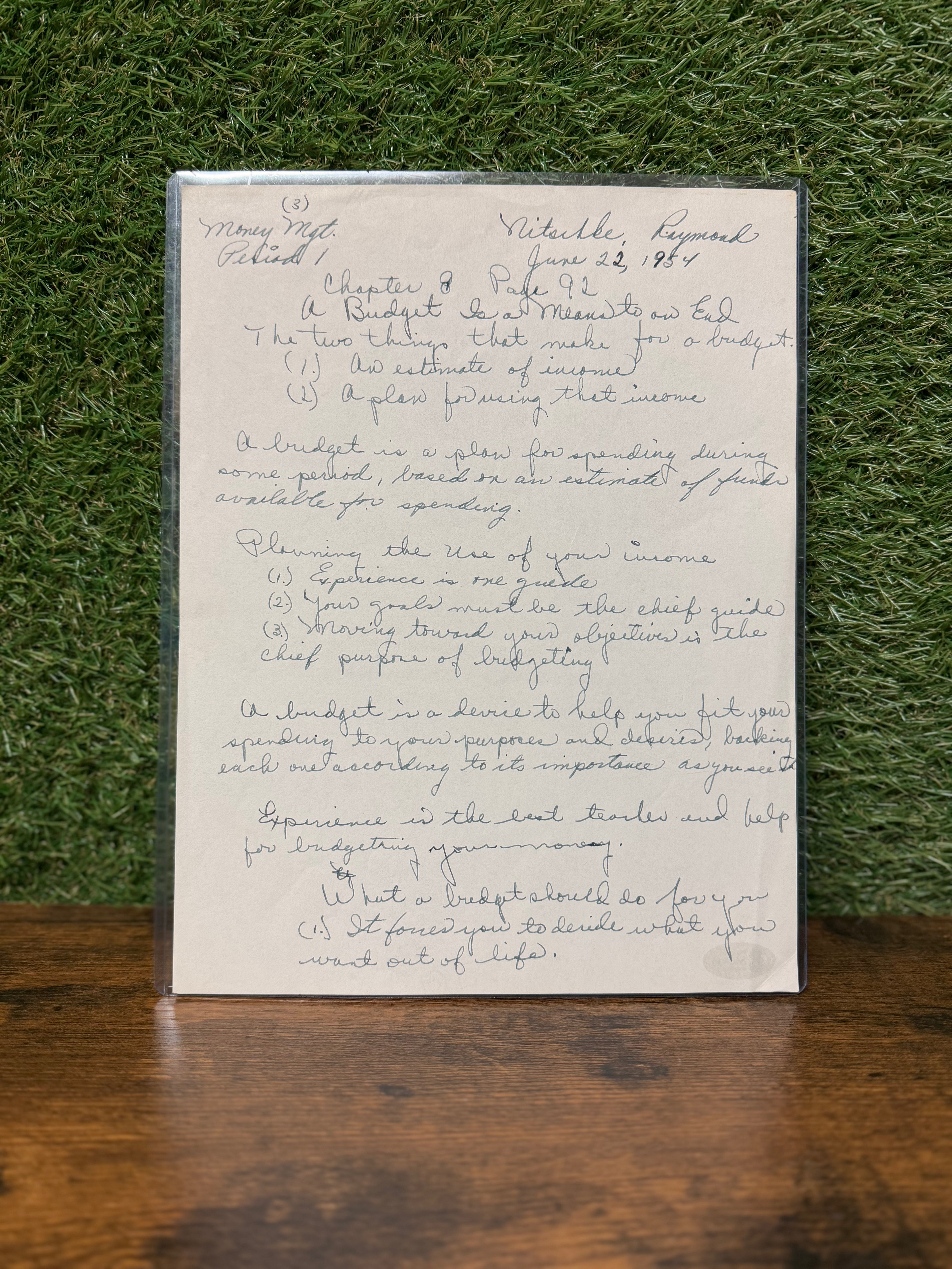 Handwritten document on a stand against a grassy background