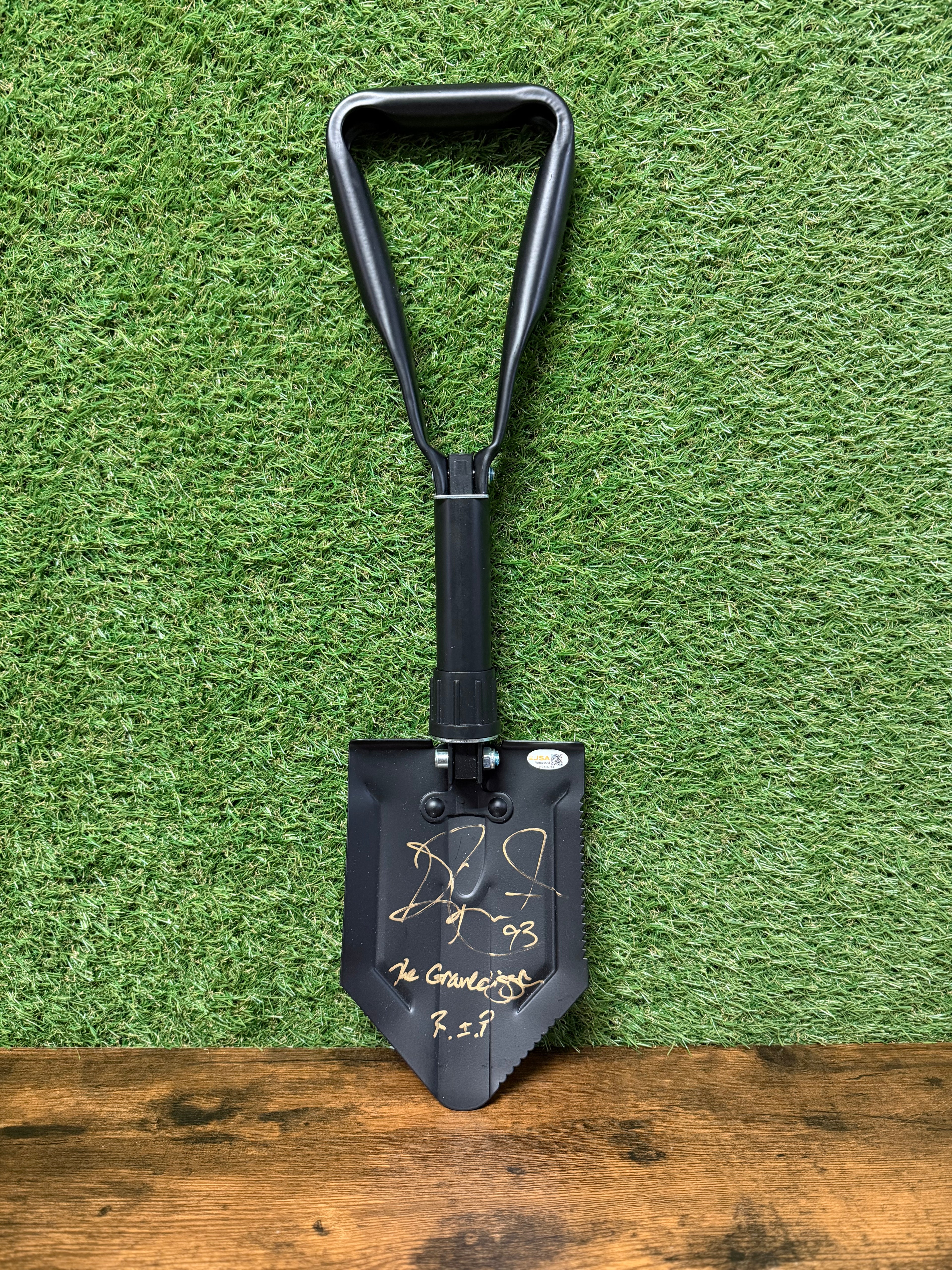 Black folding shovel with gold writing on a green grass background