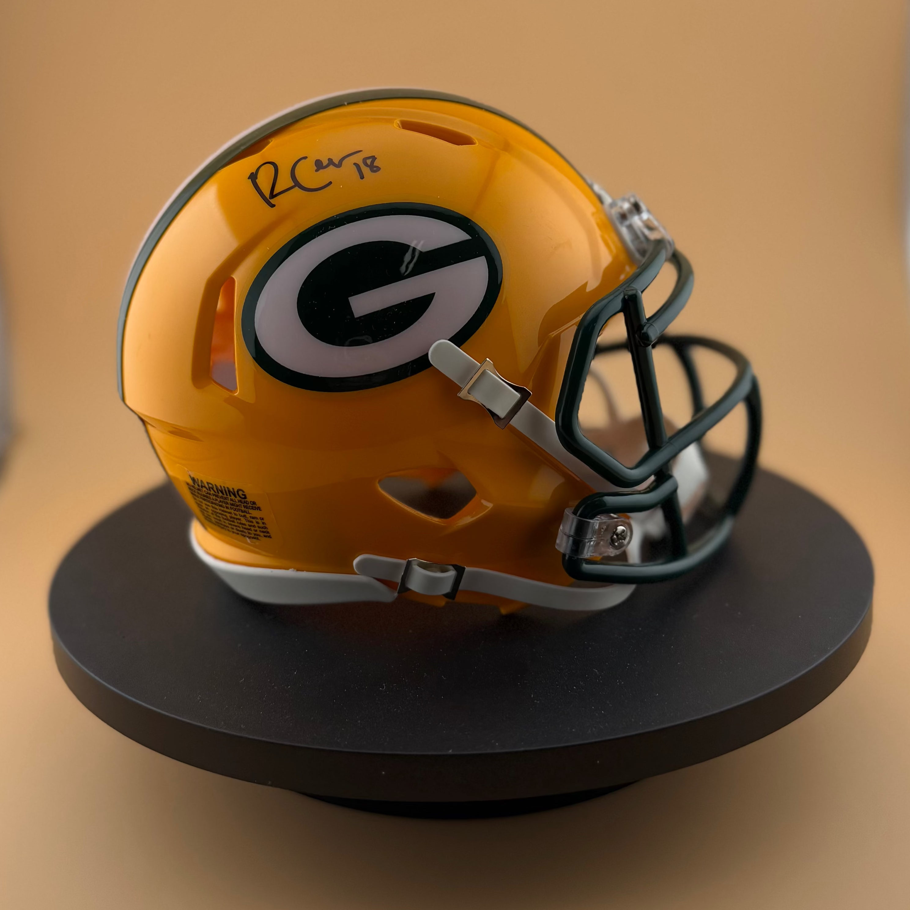 Yellow football helmet with a logo on a black stand against a beige background