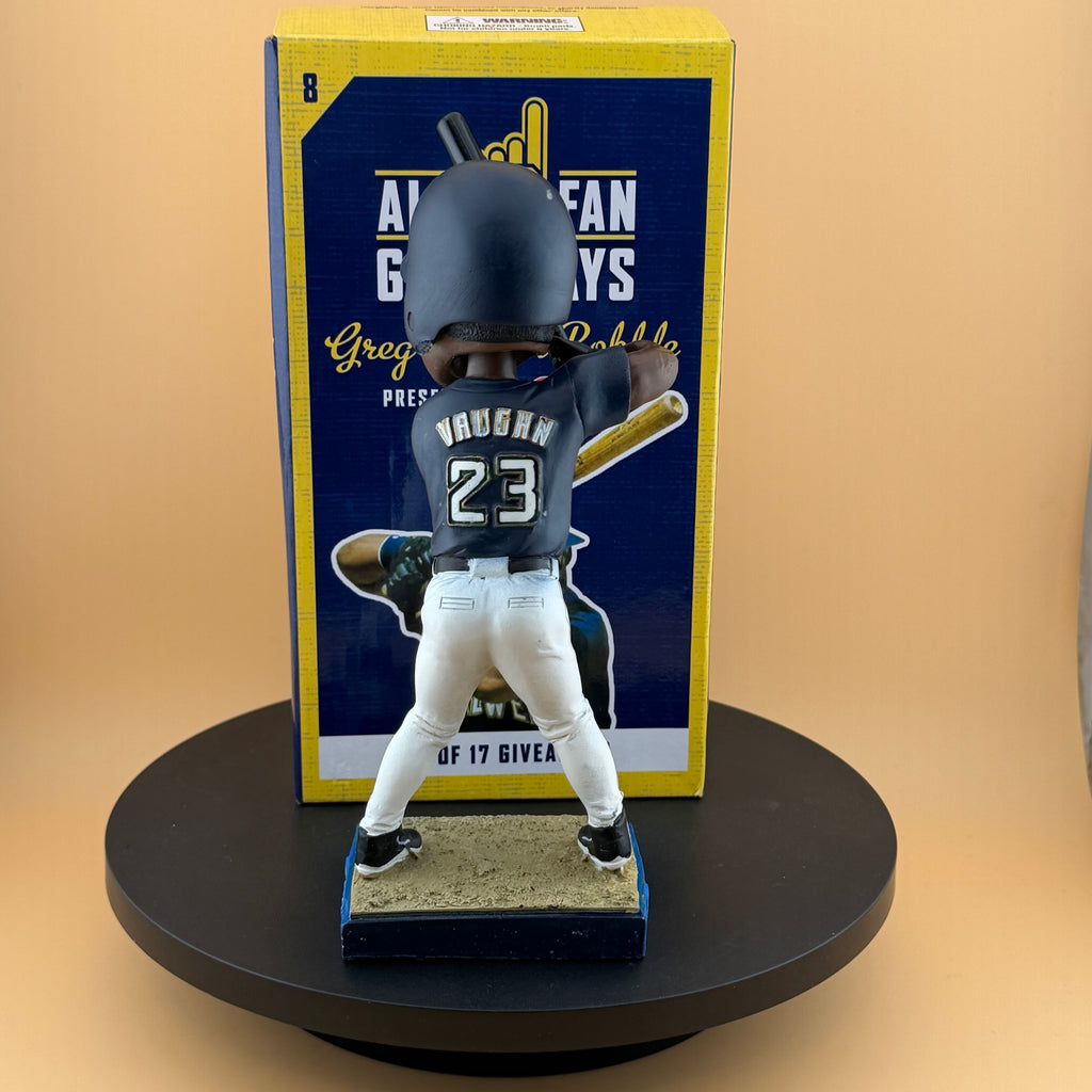 Baseball bobblehead figure with a blue uniform and bat, standing on a black platform with a branded box in the background.
